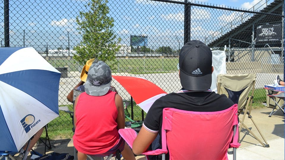 Indy 500 fans try to enjoy the race, outside looking in, hoping to catch of glimpse of action.